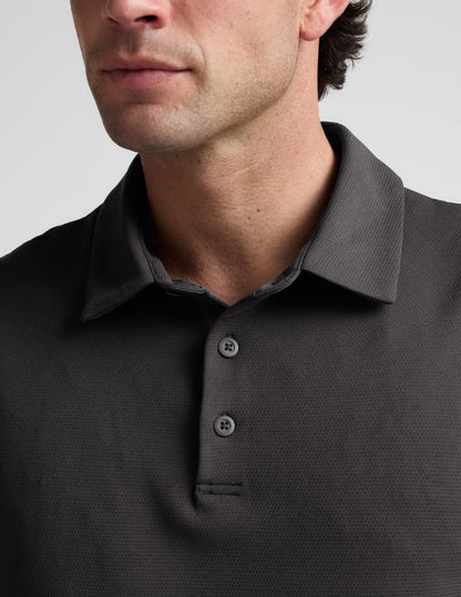 Man wearing a dark gray polo shirt against a light gray background.