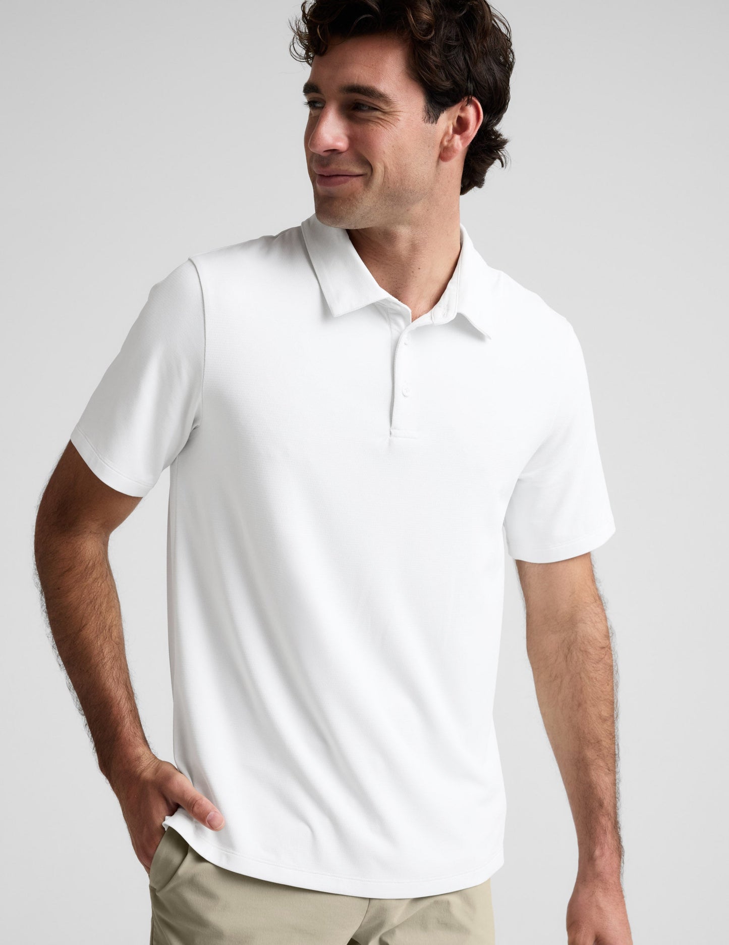 Man wearing a white polo shirt and khaki pants on a plain background.
