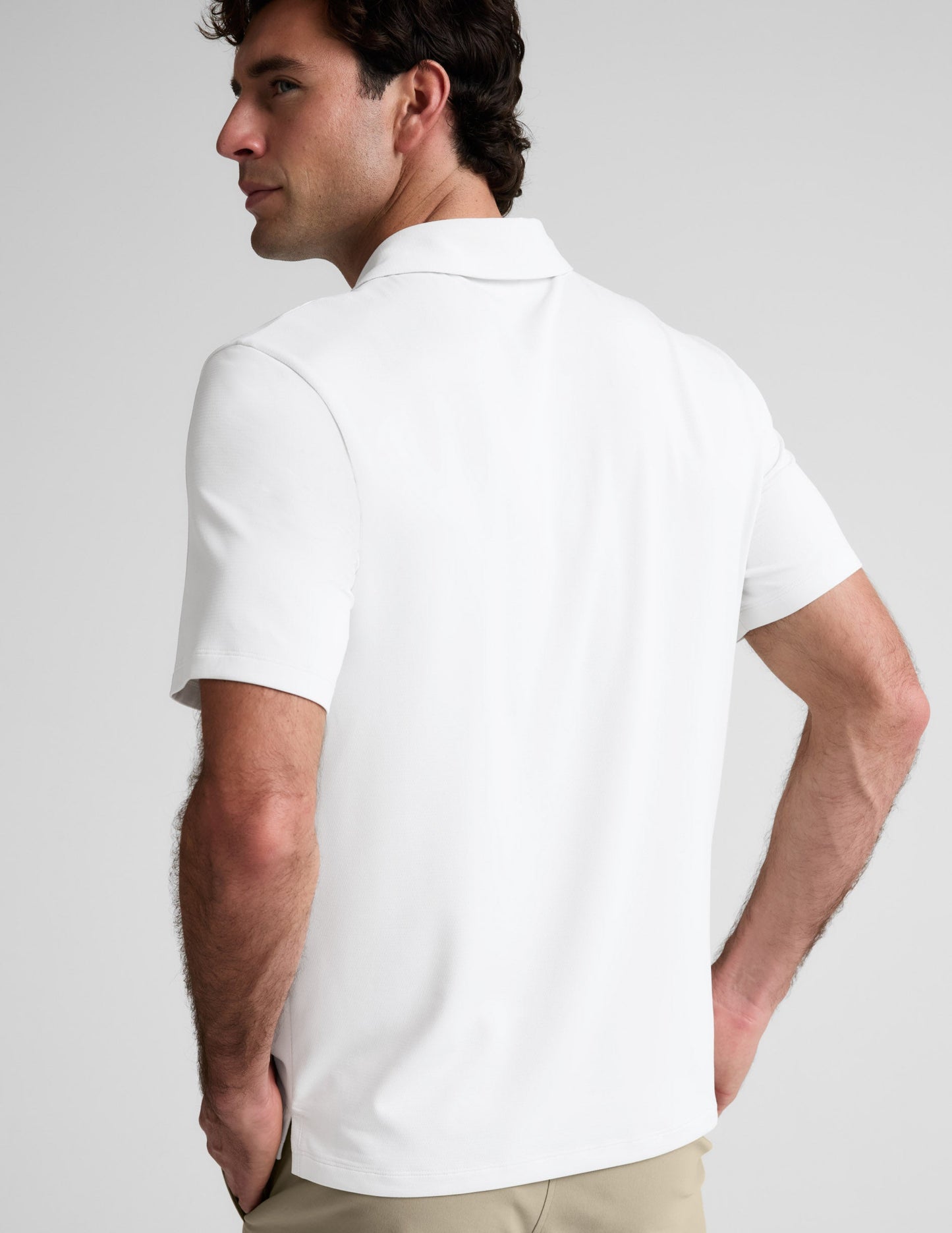 Man wearing a white polo shirt and khaki pants on a plain background.