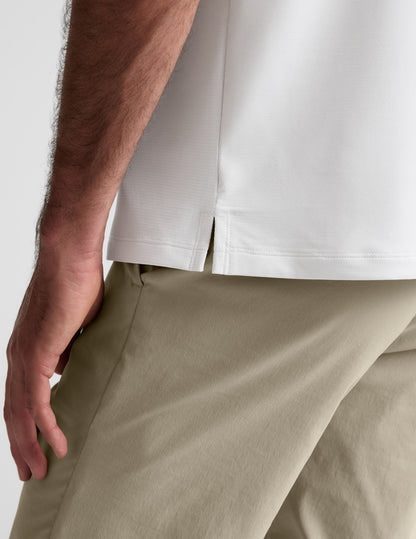 Man wearing a white polo shirt and khaki pants on a plain background.