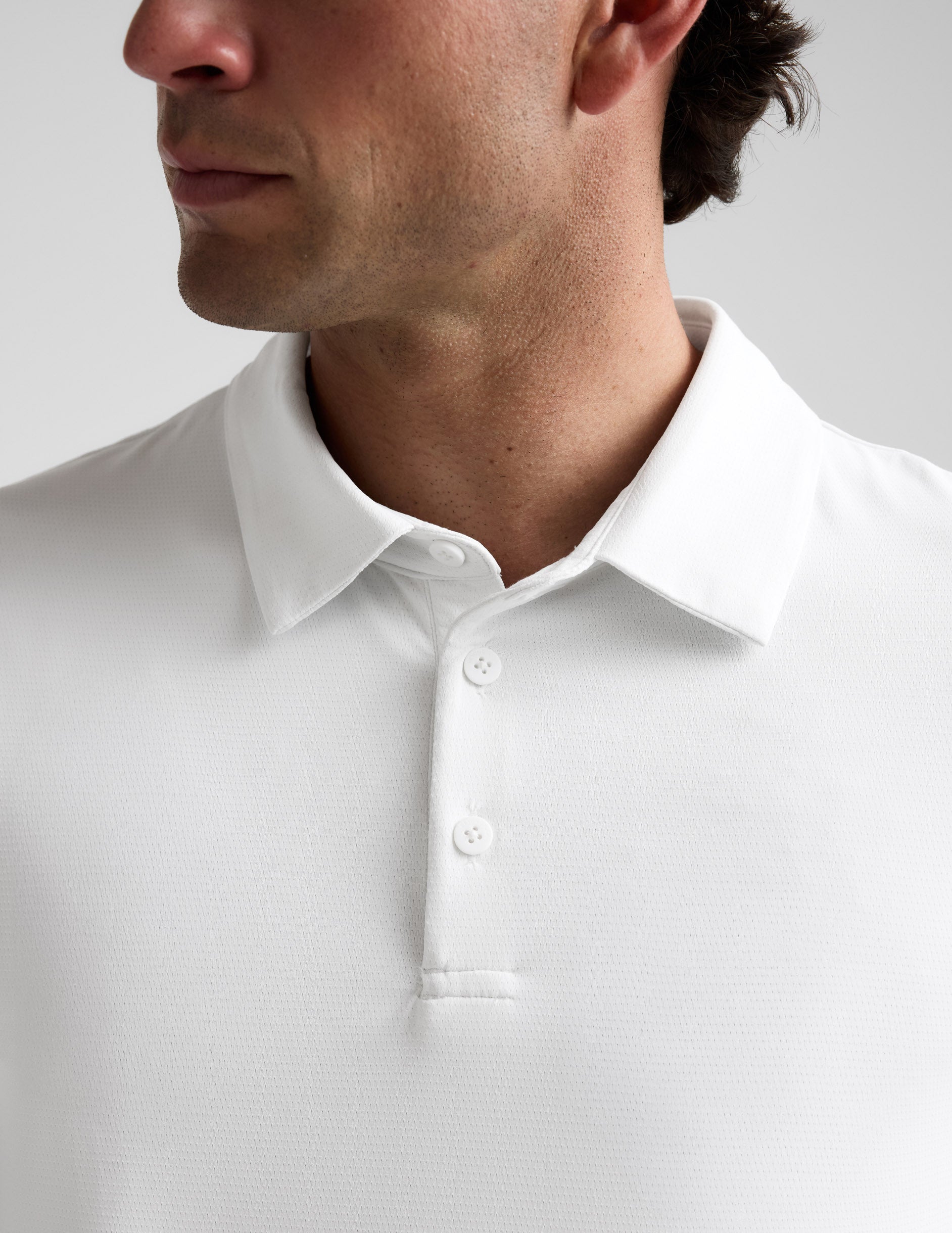 Man wearing a white polo shirt and khaki pants on a plain background.