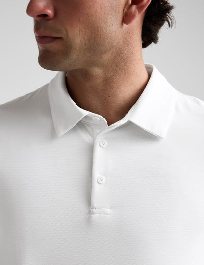 Man wearing a white polo shirt and khaki pants on a plain background.