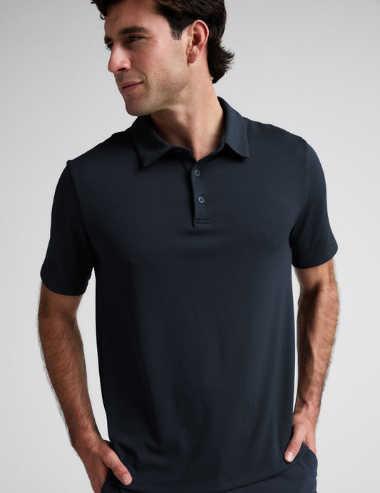 Man wearing a dark blue polo shirt and pants against a light gray background.