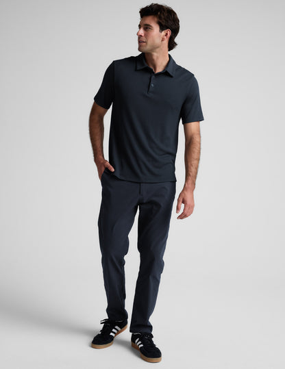 Man wearing a dark blue polo shirt and pants against a light gray background.