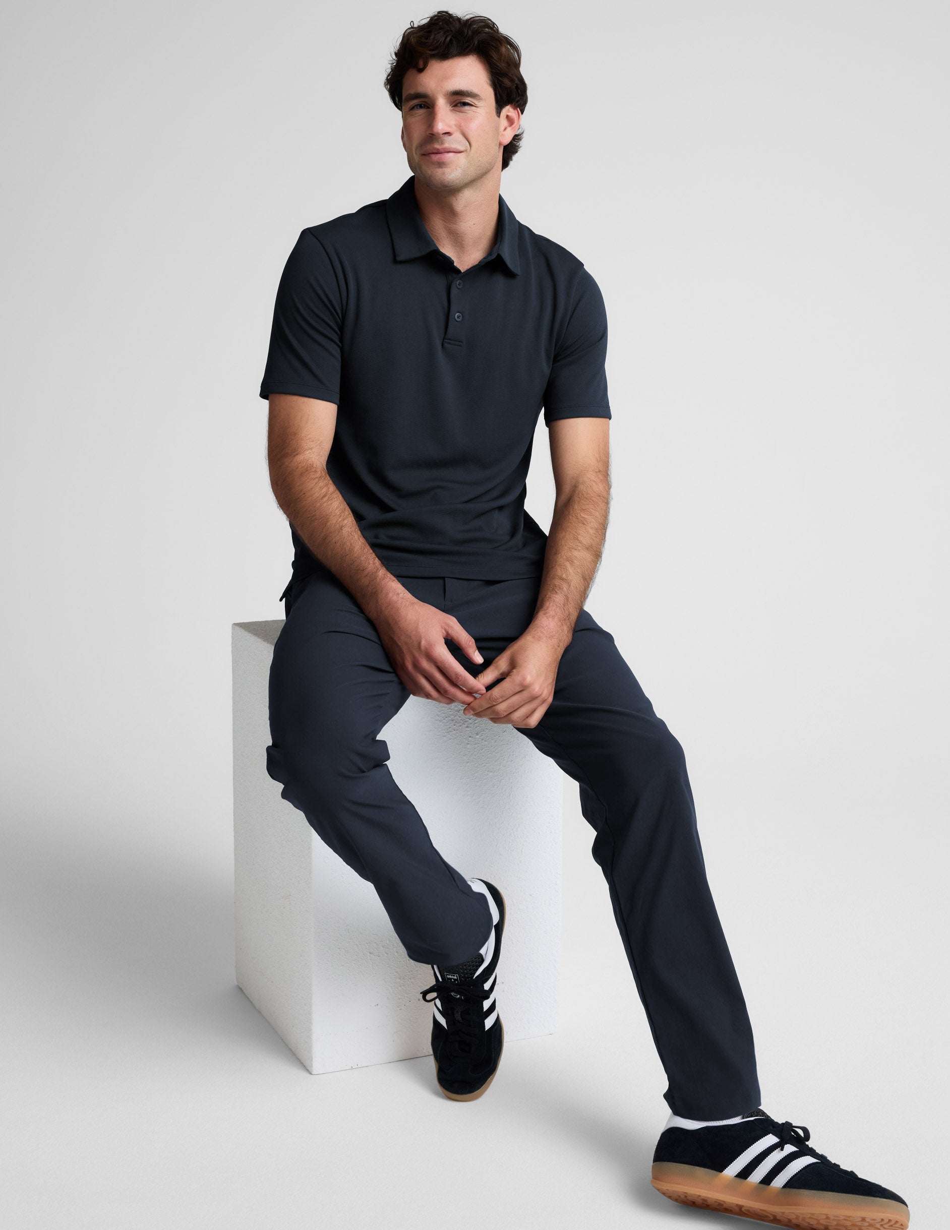 Man wearing a dark blue polo shirt and pants against a light gray background.