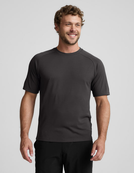 Man wearing a black athletic short sleeve top and black shorts against a plain background.