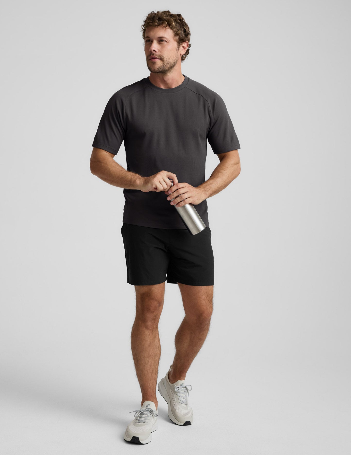 Man wearing a black athletic short sleeve top and black shorts against a plain background.