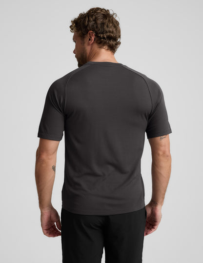 Man wearing a black athletic short sleeve top and black shorts against a plain background.