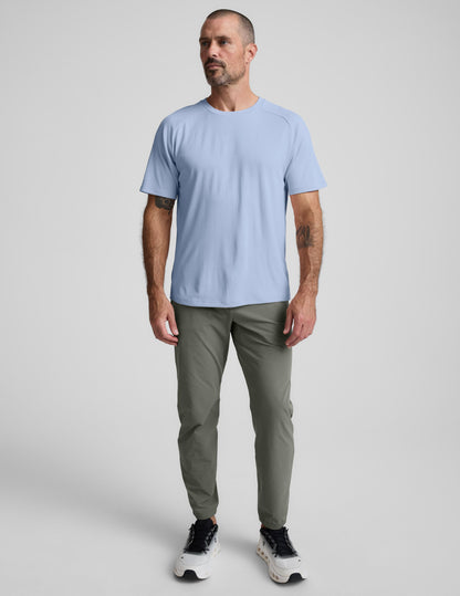 Man wearing a blue t-shirt and pants against a plain background.