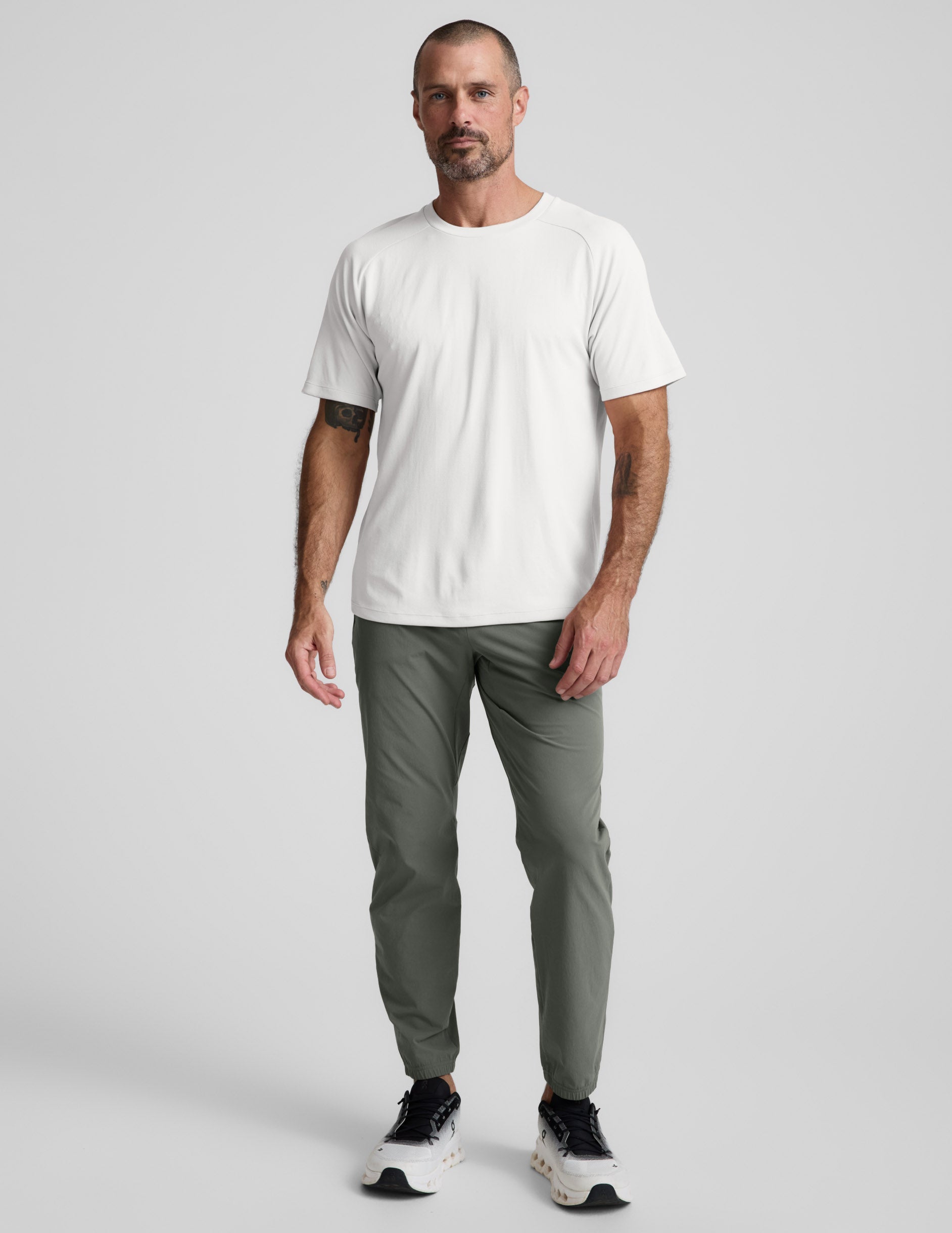 Man wearing a white t-shirt and green pants on a light gray background.