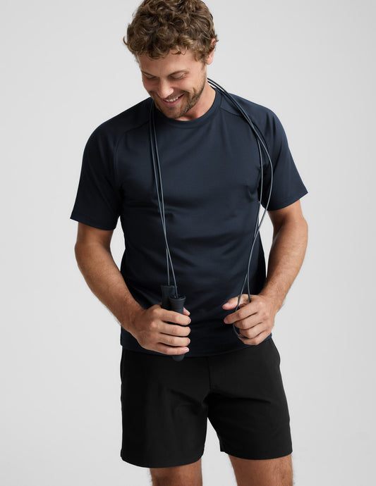 Man holding a jump rope wearing a blue t-shirt and shorts on a light gray background.
