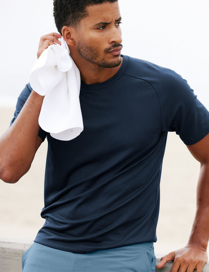 Man in a blue athletic t-shirt and shorts with a towel, standing outdoors.