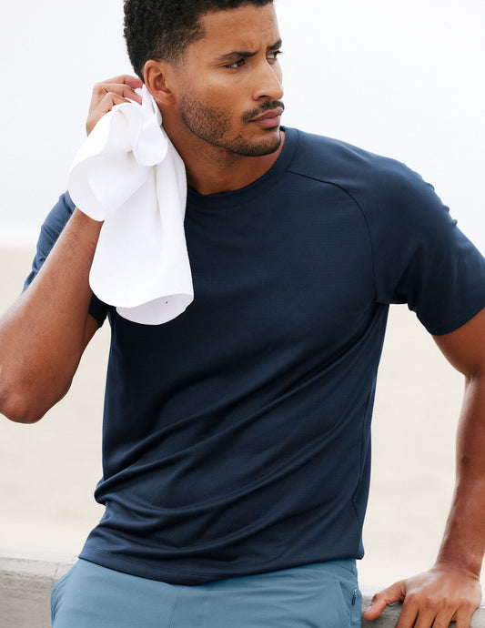 Man in a blue athletic t-shirt and shorts with a towel, standing outdoors.