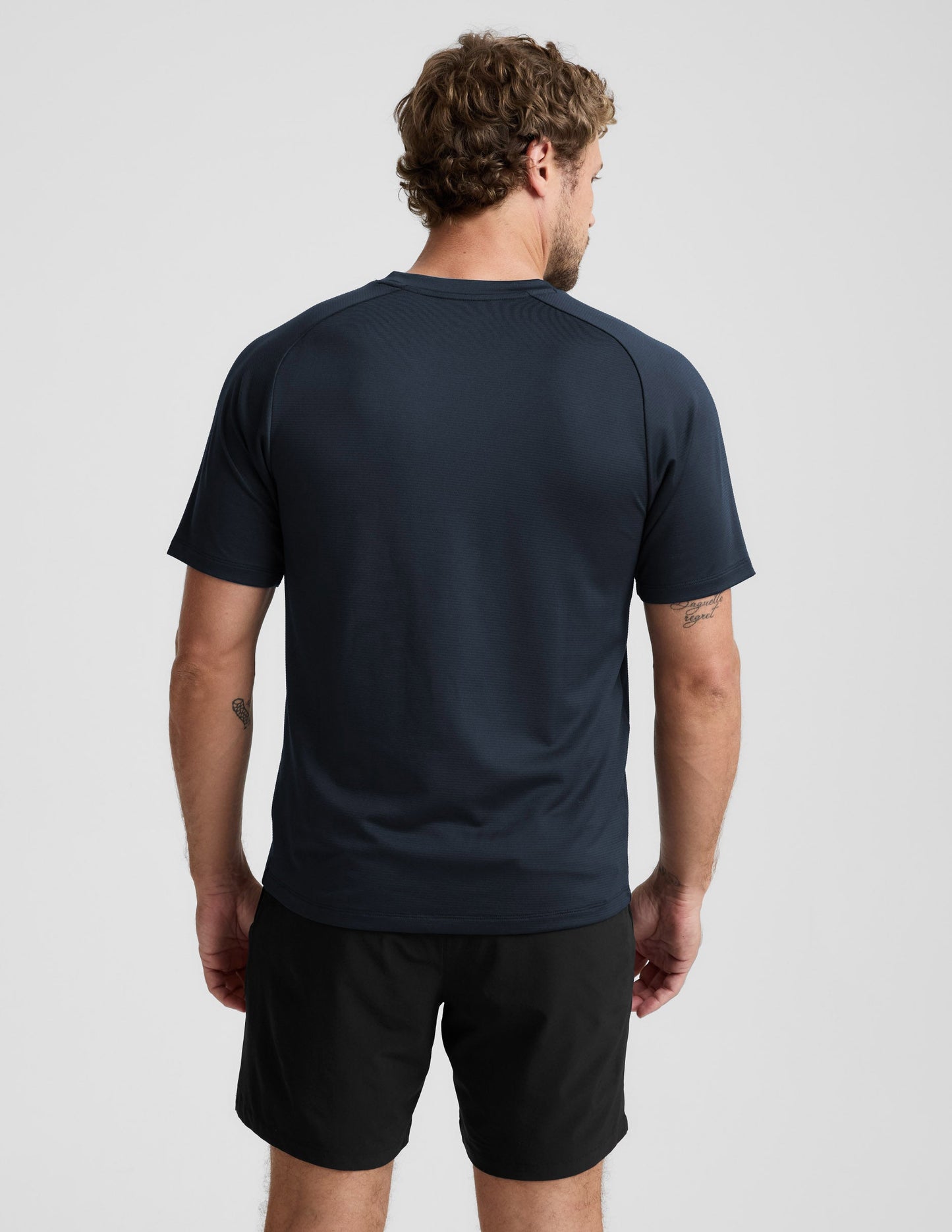 Man wearing a navy athletic shirt and black shorts on a light gray background