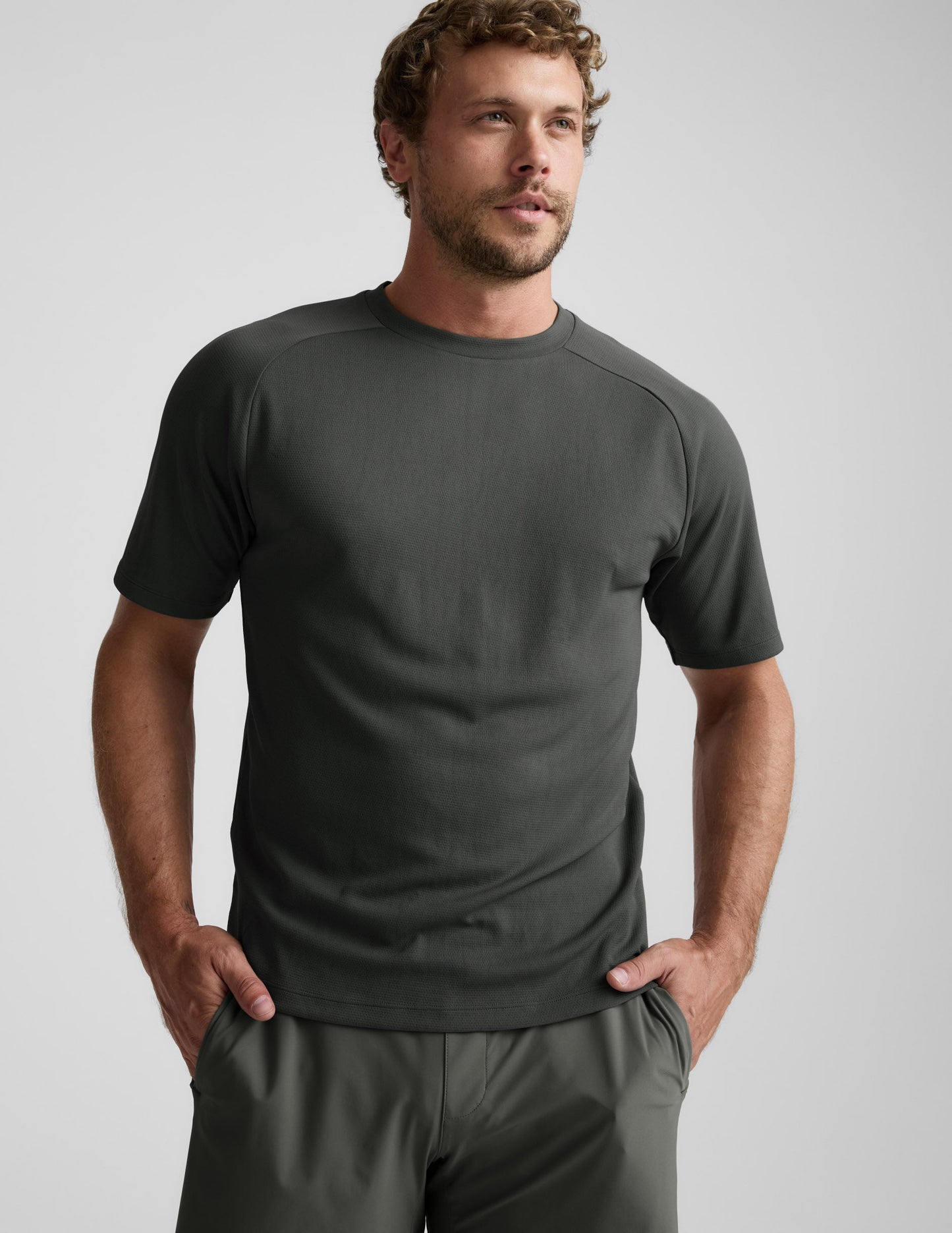 Man wearing a dark green t-shirt and shorts on a light gray background.