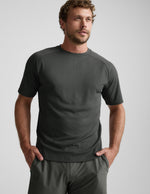 Man wearing a dark green t-shirt and shorts on a light gray background.
