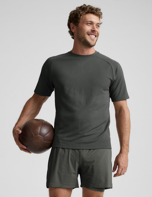 Man wearing a dark green t-shirt and shorts on a light gray background.