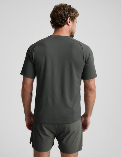 Man wearing a dark green t-shirt and shorts on a light gray background.