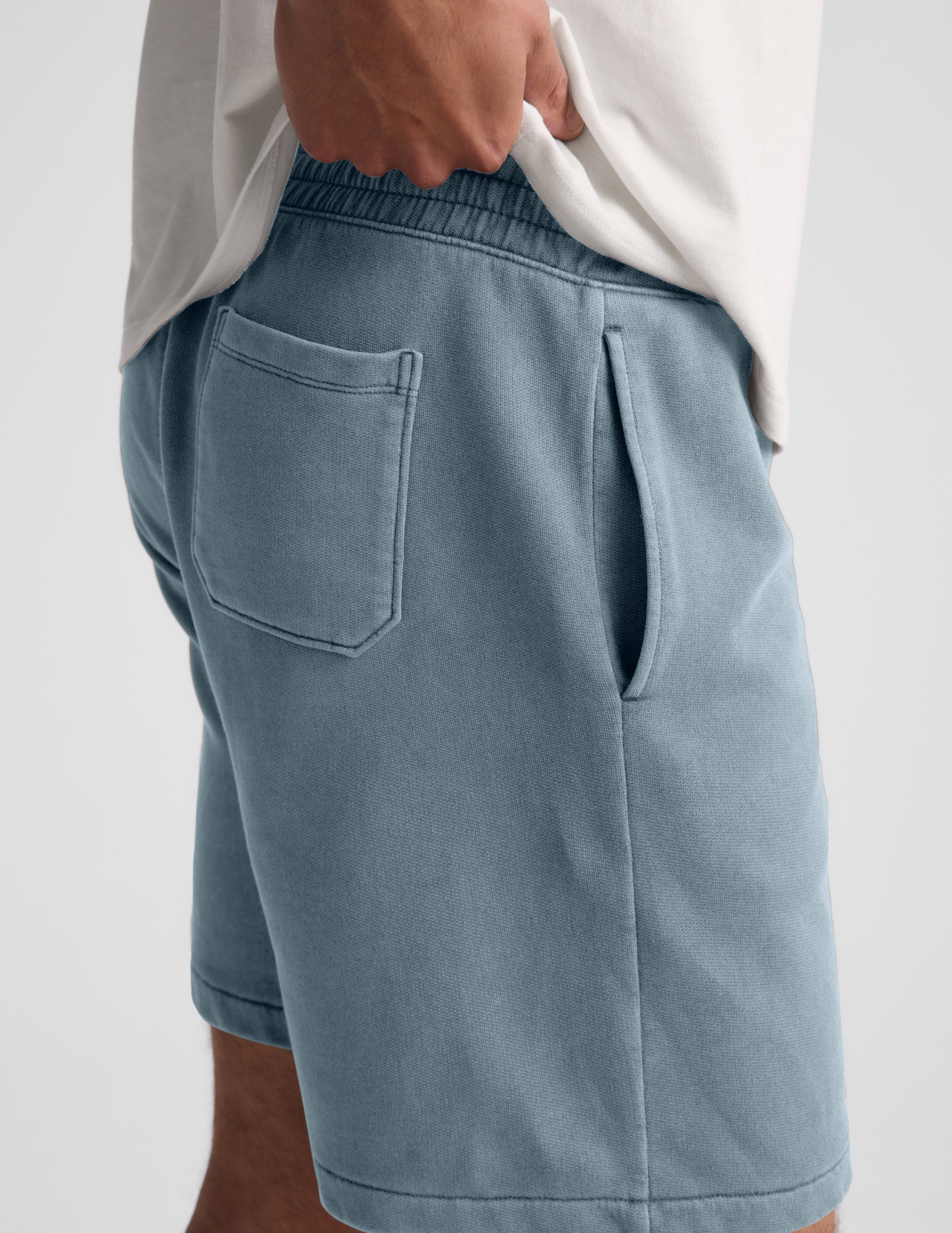 Man wearing Blue Beach Washed Terry Men's Short with a white t-shirt, showing side slant and back patch pocket details.