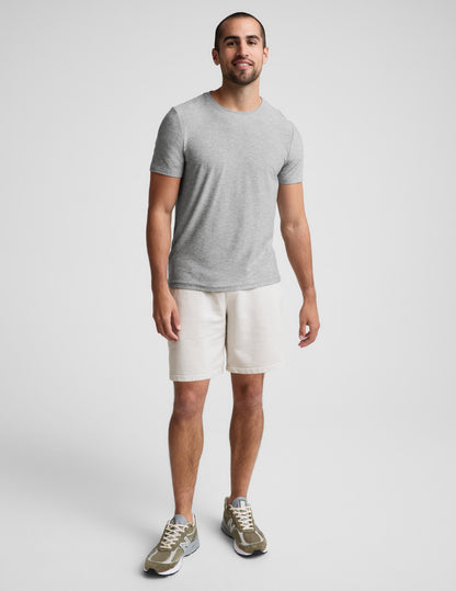 Man wearing Cream Beach Washed Terry Men's Short with an elastic waistband, styled with a grey t-shirt and olive sneakers.
