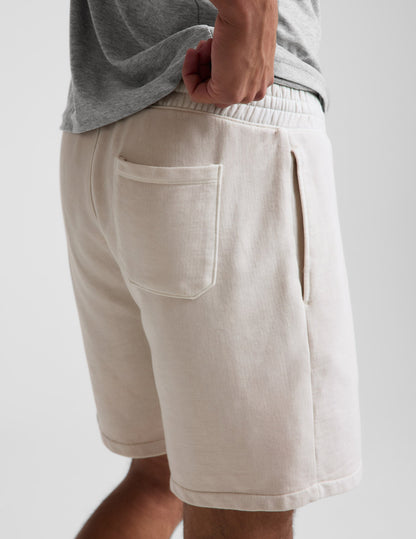 Man wearing Cream Beach Washed Terry Men's Short paired with a grey t-shirt, featuring a back patch pocket and side pocket.