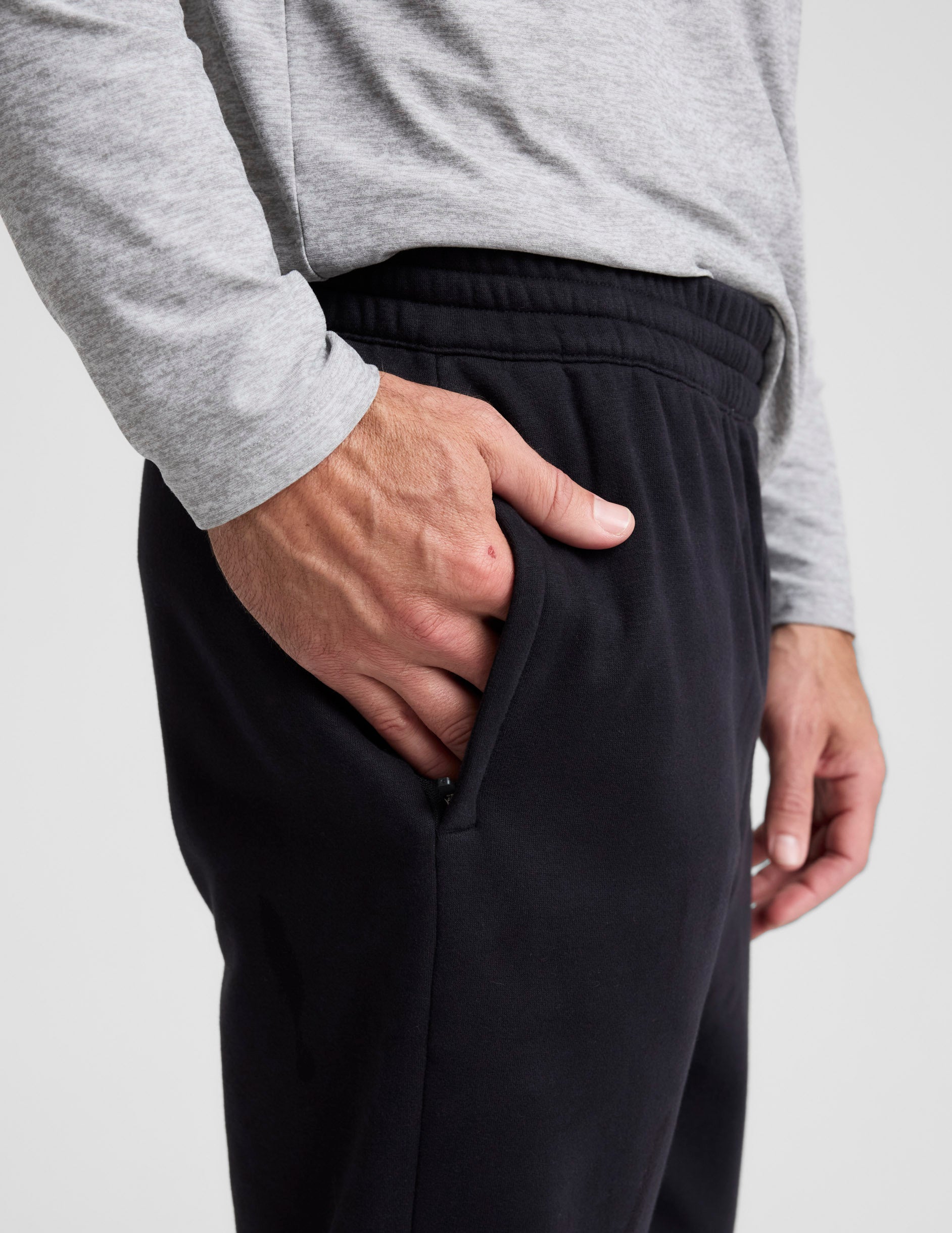 Close-up of black Classic Fleece Men's Jogger showing the elastic waistband and a hand in the side zipper pocket.