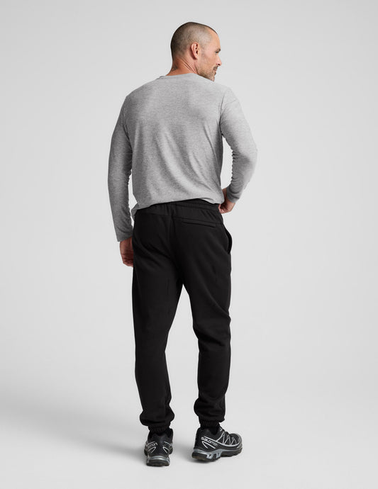 Rear view of a man in black Classic Fleece Men's Joggers with a relaxed fit, elastic waistband, and cuffed ankles.