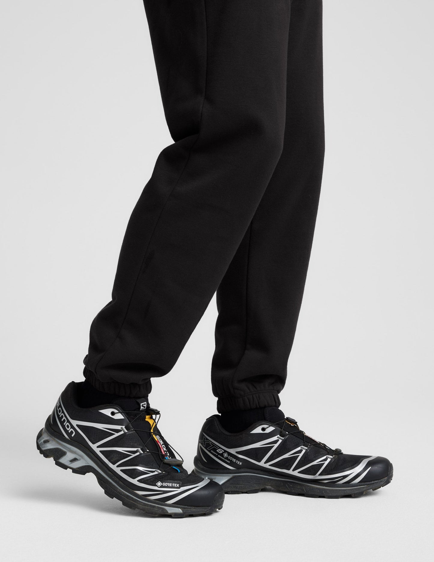 Profile view of black Classic Fleece Men's Joggers showing the relaxed fit and gathered elastic cuffs at the ankle.