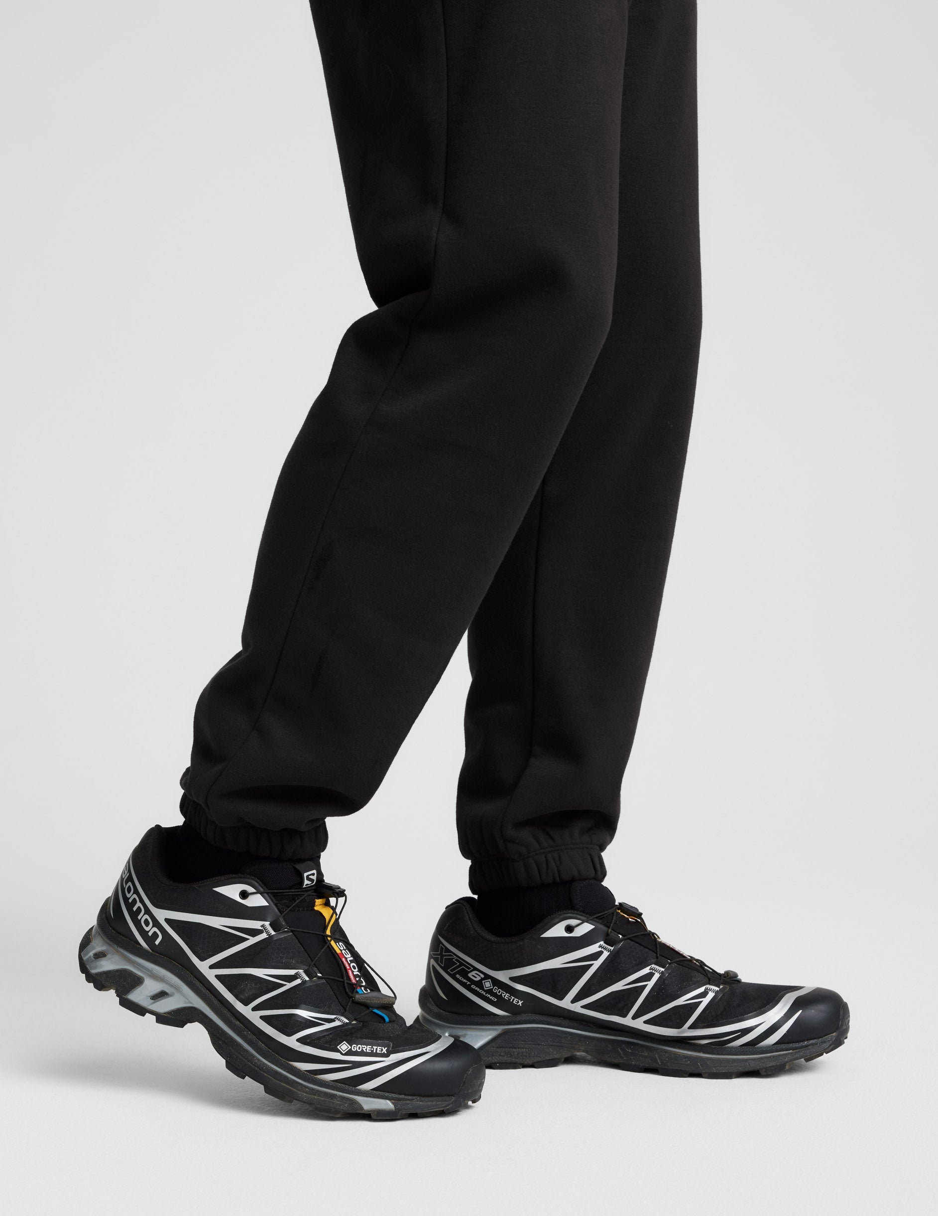 Profile view of black Classic Fleece Men's Joggers showing the relaxed fit and gathered elastic cuffs at the ankle.