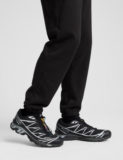 Profile view of black Classic Fleece Men's Joggers showing the relaxed fit and gathered elastic cuffs at the ankle.