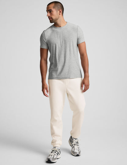 A man wears off-white Classic Fleece Men's Joggers with a relaxed fit, elastic cuffs, and a gray t-shirt.