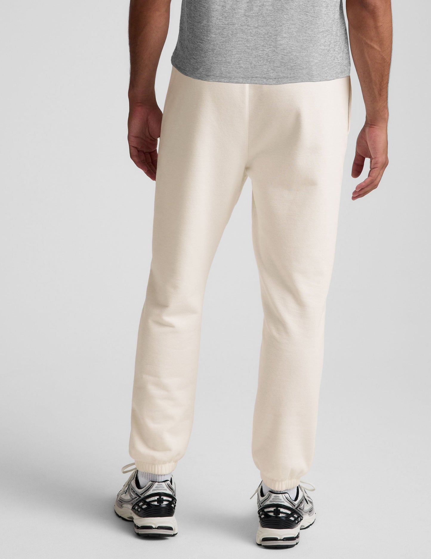 Back view of a man wearing cream Classic Fleece Men's Joggers featuring a relaxed fit and gathered elastic cuffs.