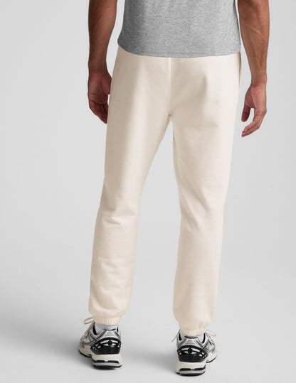 Back view of a man wearing cream Classic Fleece Men's Joggers featuring a relaxed fit and gathered elastic cuffs.