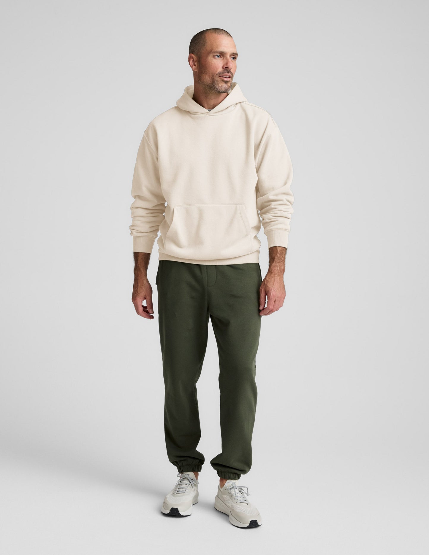 Man wearing Olive Classic Fleece Men's Jogger in a relaxed fit, paired with a cream hoodie and white sneakers.