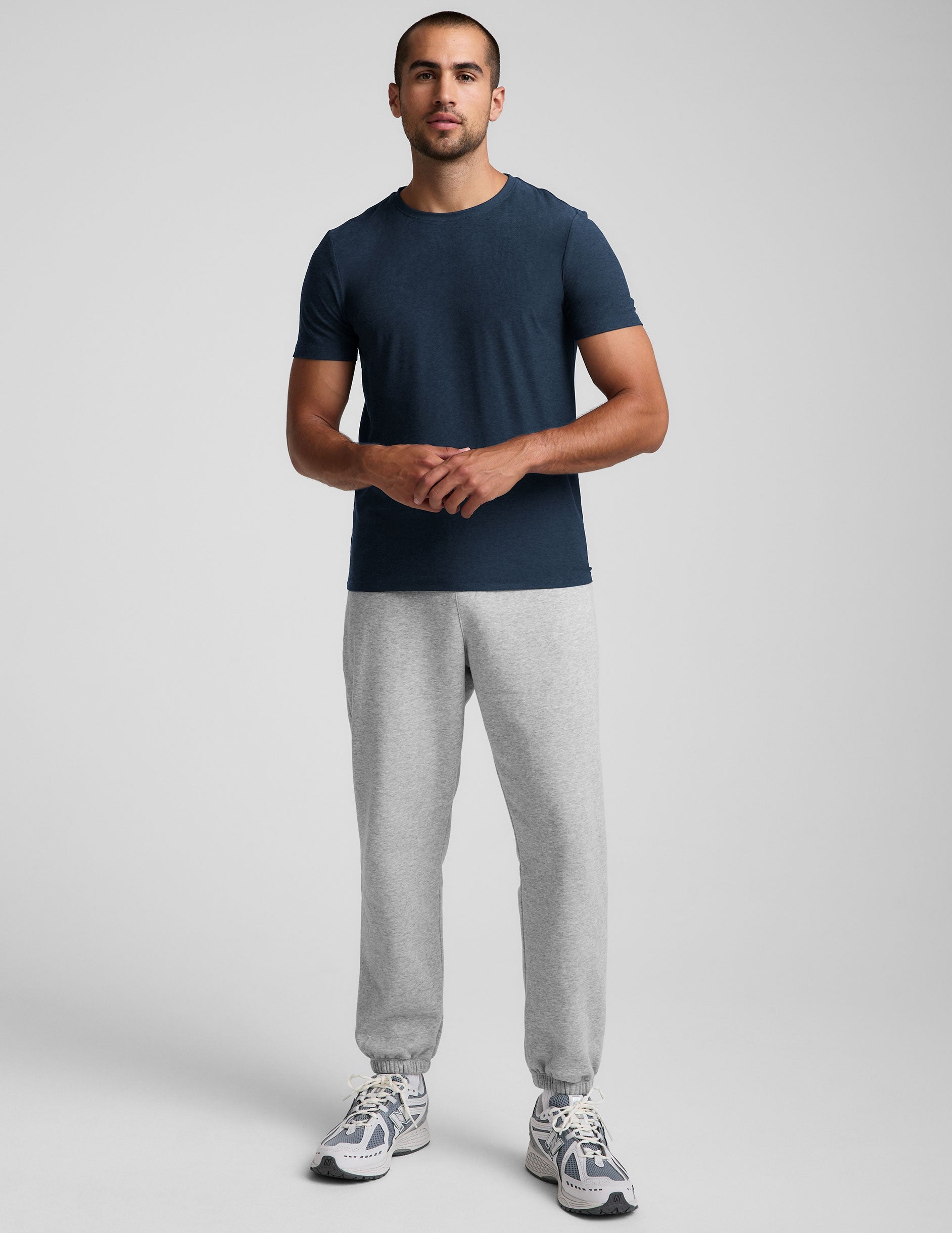 A man wears the light grey marled Classic Fleece Men's Jogger with a relaxed fit, cuffed ankles, and side zipper pockets.