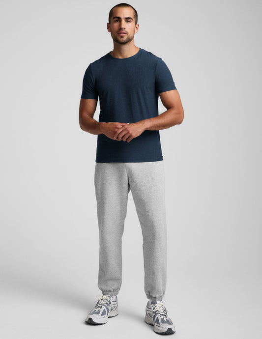 A man wears the light grey marled Classic Fleece Men's Jogger with a relaxed fit, cuffed ankles, and side zipper pockets.