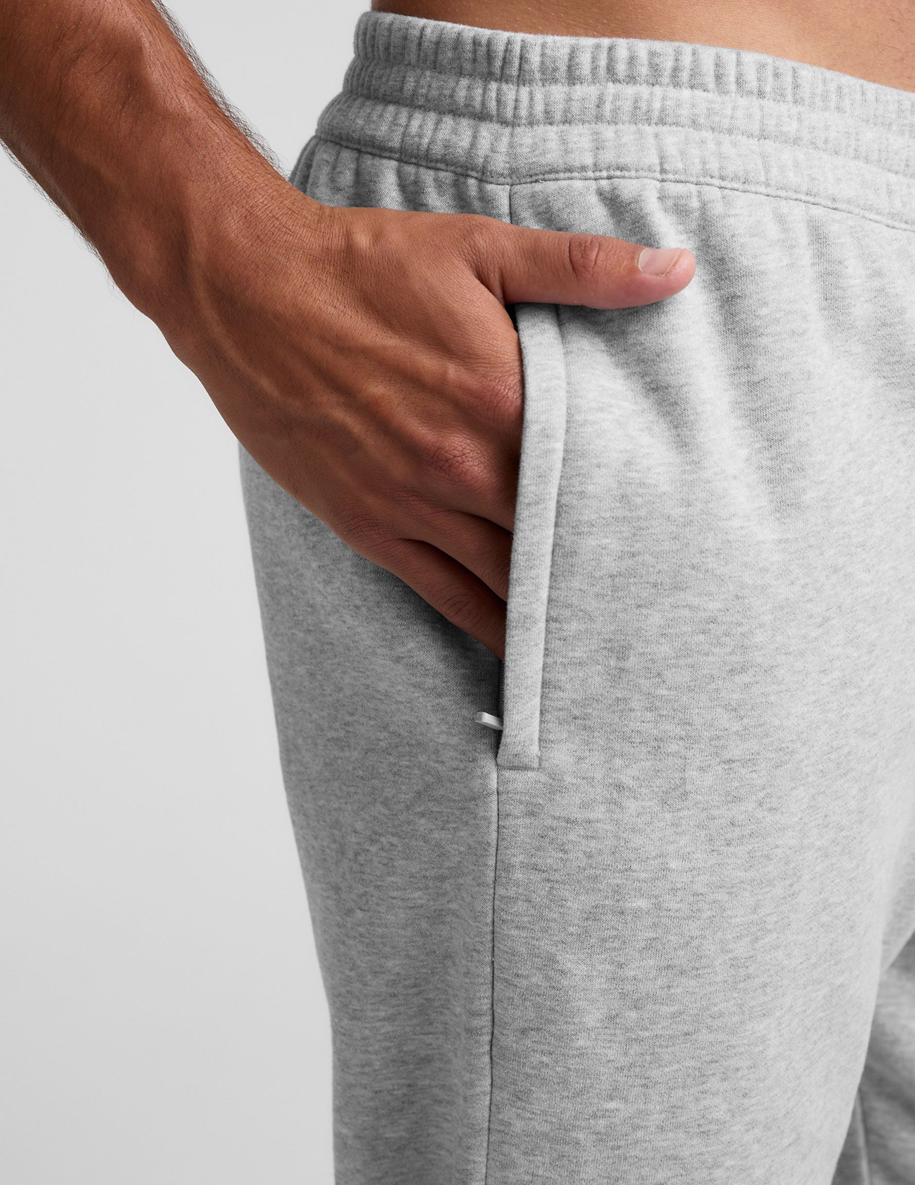 Close-up of a hand in the side zipper pocket of the grey marled Classic Fleece Men's Jogger with an elastic waistband.