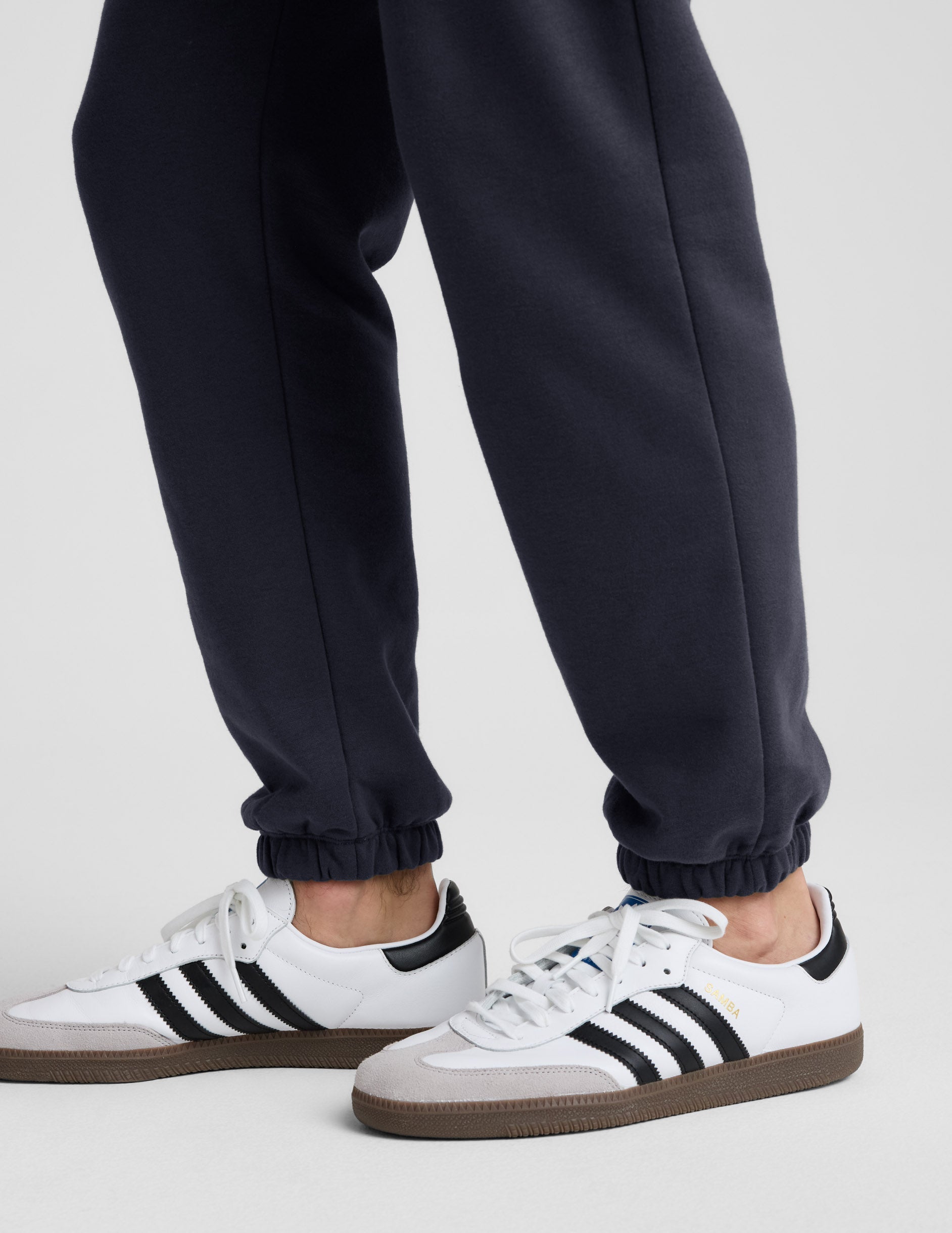 Classic Fleece Men's Jogger in dark gray, showing the relaxed fit and gathered elastic cuffs above white sneakers.