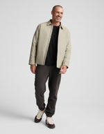 Smiling man wearing dark Classic Fleece Men's Jogger with elastic cuffs, styled with a beige jacket and sneakers.