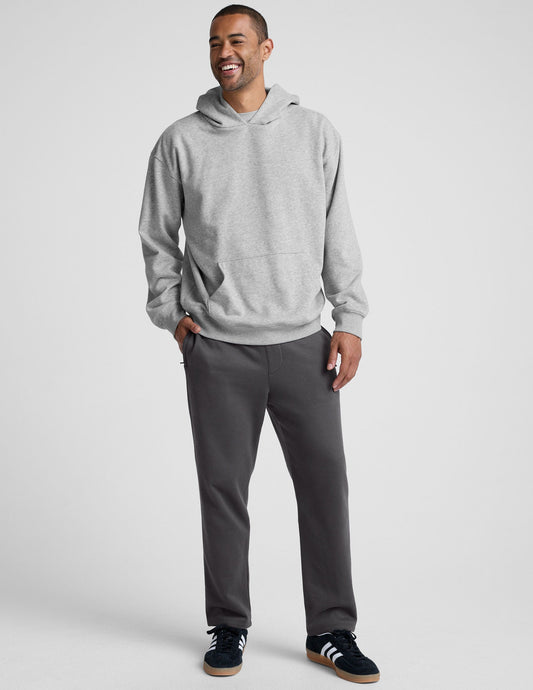 A smiling man wears dark gray LuxeFleece Men's Straight Leg Pants with a light gray hoodie and black sneakers.