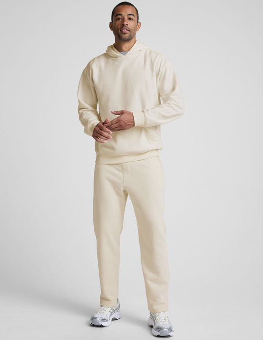 A man wears the cream LuxeFleece Men's Straight Leg Pant with a matching hoodie and silver sneakers against a gray backdrop.