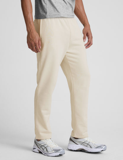 Side view of a man wearing cream LuxeFleece Men's Straight Leg Pant with zippered pockets and a comfortable relaxed fit.