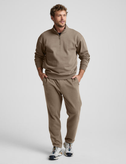 Man wearing brown LuxeFleece Men's Straight Leg Pant, featuring a straight fit and zippered pockets, in a studio setting.