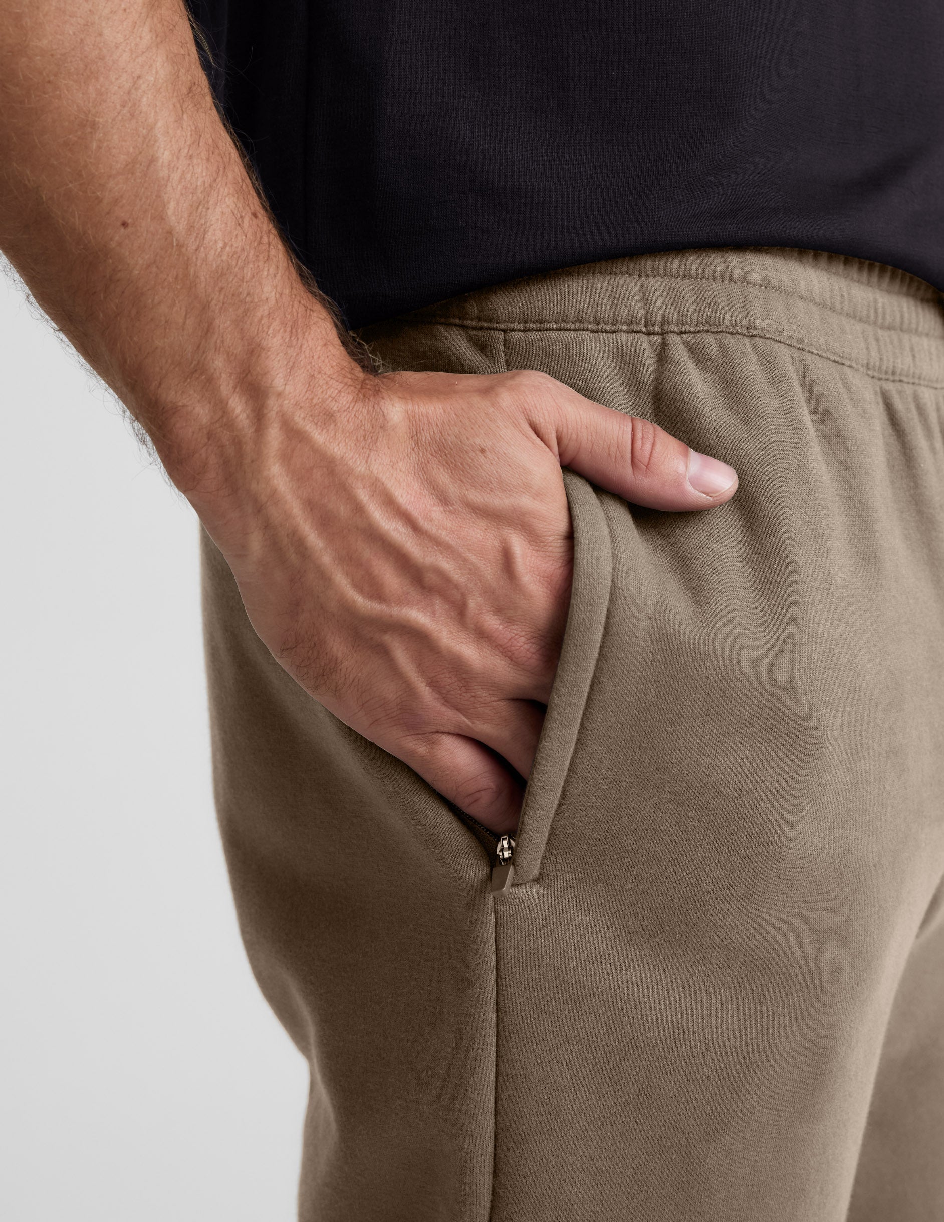 A hand in the zippered side pocket of the brown LuxeFleece Men's Straight Leg Pant showing the soft fabric texture.