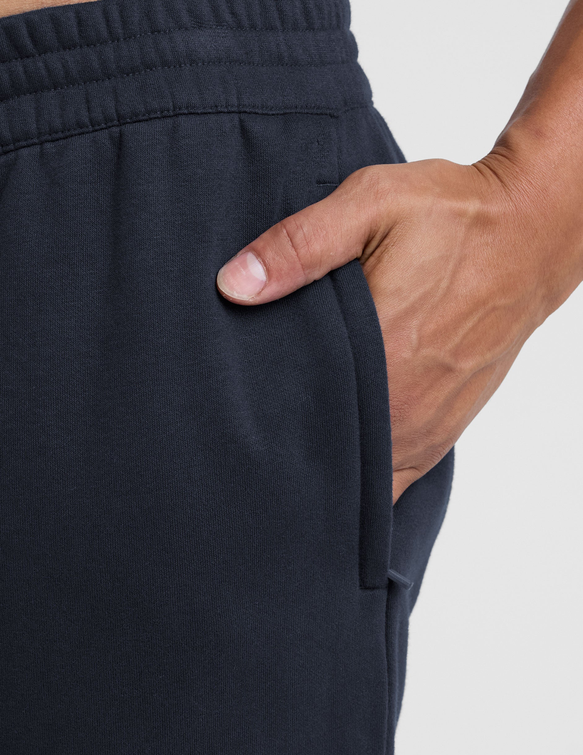 Close-up of navy LuxeFleece Men's Straight Leg Pant showing the elastic waistband and a hand in the side zippered pocket.
