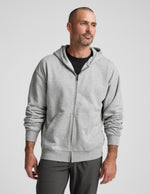 Man wearing a gray full zip hoodie and dark gray pants on a plain background.