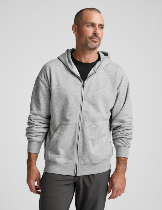 Man wearing a gray full zip hoodie and dark gray pants on a plain background.