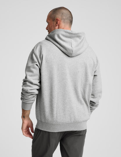 Man wearing a gray full zip hoodie and dark gray pants on a plain background.