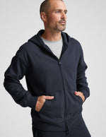 Man wearing a navy blue full zip hoodie and shorts on a plain background.