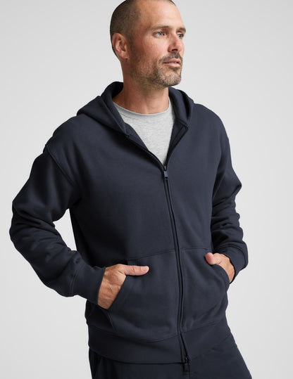 Man wearing a navy blue full zip hoodie and shorts on a plain background.